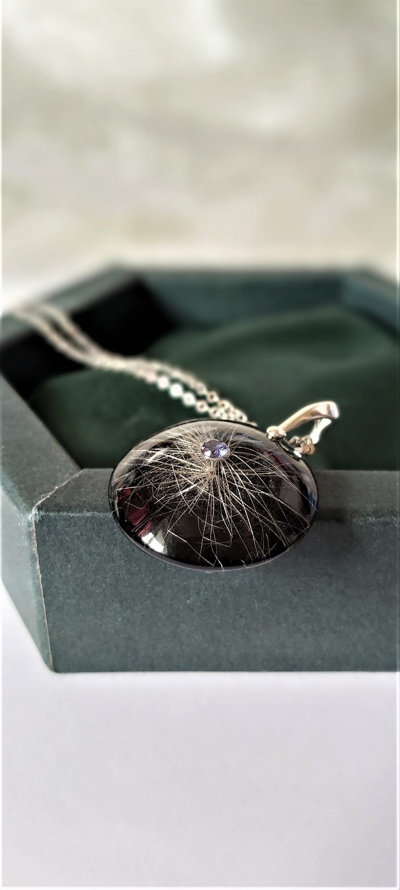 May include: A silver necklace with a black round pendant containing a small amount of hair and a purple gemstone in the center.