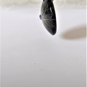 May include: A silver chain necklace with a black heart-shaped pendant containing a small blue gemstone and white hair.