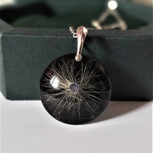 May include: A silver pendant necklace with a round black resin charm containing a small amount of hair and a purple gemstone in the center.