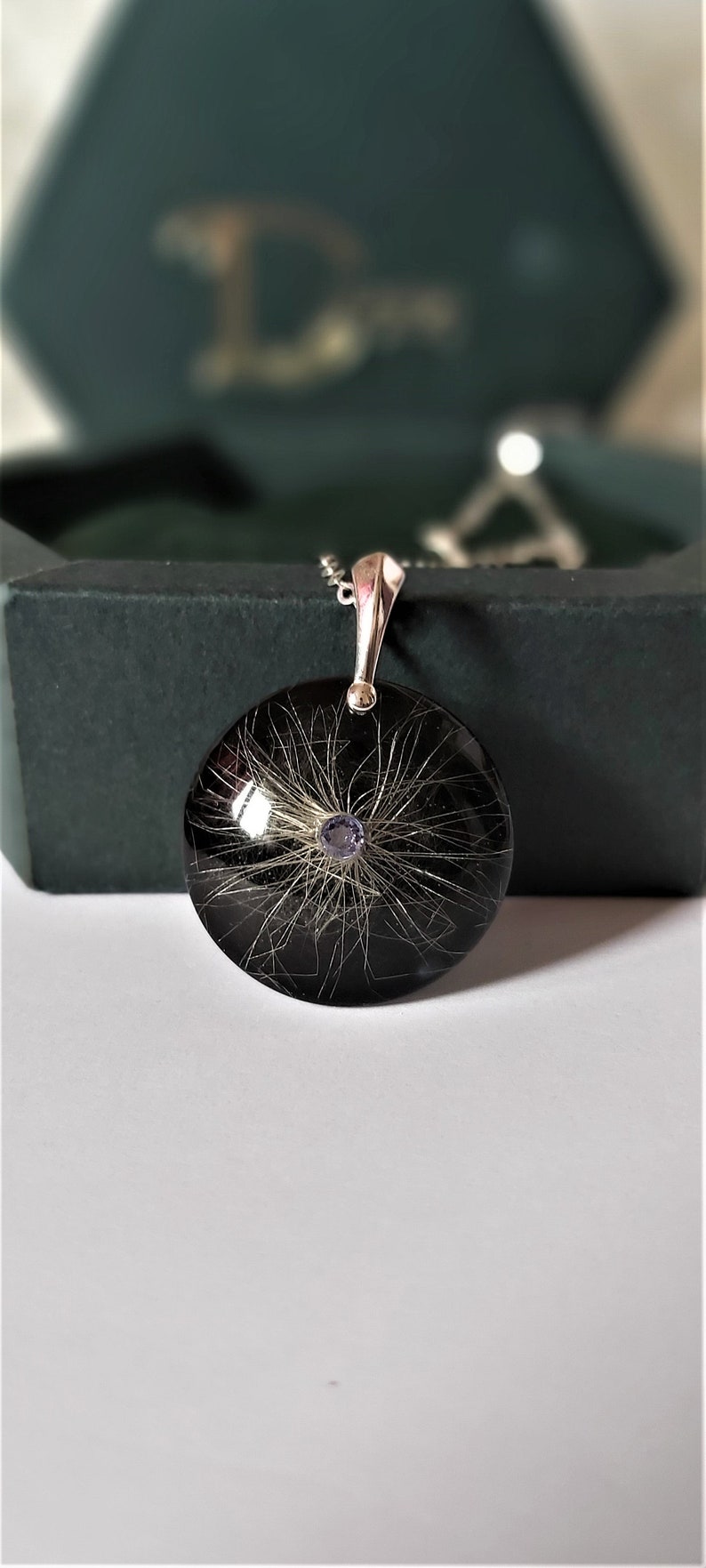 May include: A silver pendant necklace with a round black resin charm containing a small amount of hair and a purple gemstone in the center.