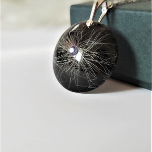 May include: A silver pendant necklace with a black resin round charm containing a small amount of hair and a small blue gemstone.