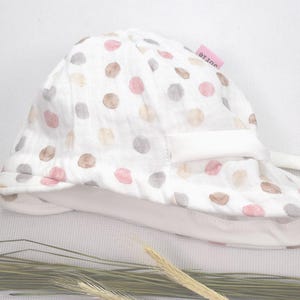 Könnte beinhalten: Weißer Sonnenhut mit rosa und braunen Punkten. Der Hut hat einen weißen Rand und eine weiße Schleife.