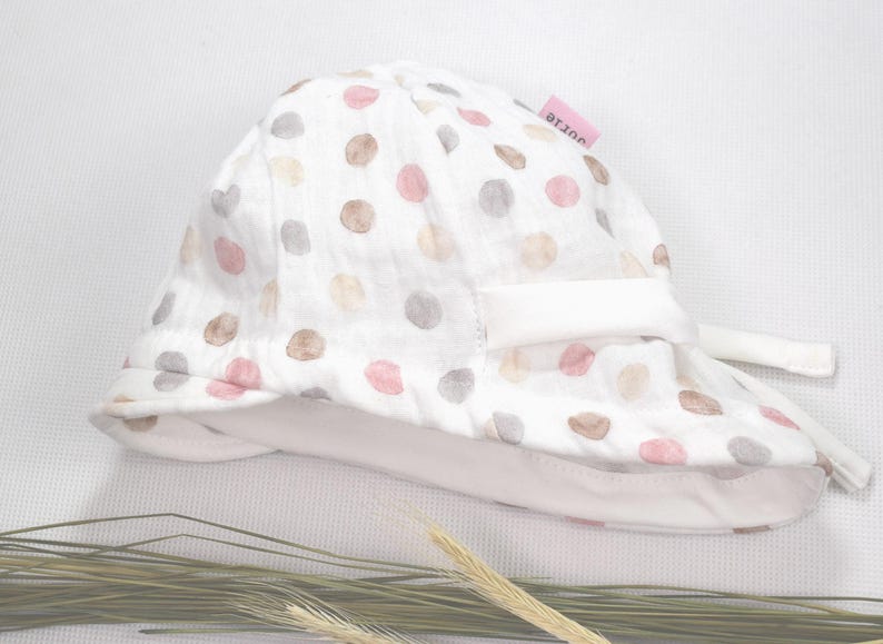 Könnte beinhalten: Weißer Sonnenhut mit rosa und braunen Punkten. Der Hut hat einen weißen Rand und eine weiße Schleife.
