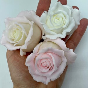 Pu&ograve; includere: Tre rose artificiali, una bianca e due rosa, sono mostrate in una mano. Le rose sono fatte di un materiale morbido e flessibile e hanno un aspetto realistico.
