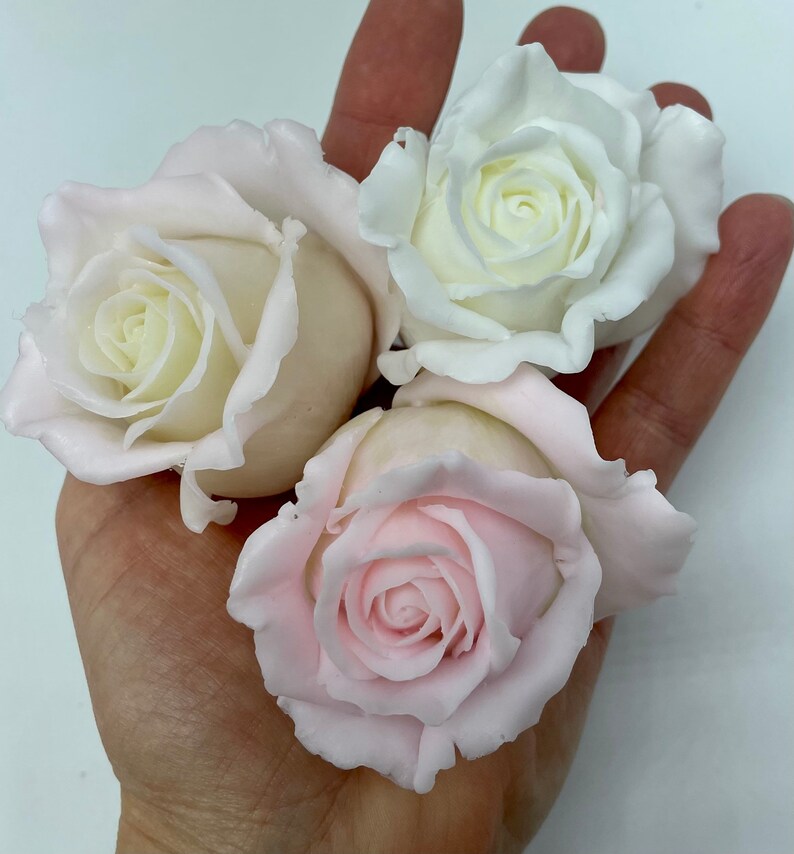 Pu&ograve; includere: Tre rose artificiali, una bianca e due rosa, sono mostrate in una mano. Le rose sono fatte di un materiale morbido e flessibile e hanno un aspetto realistico.