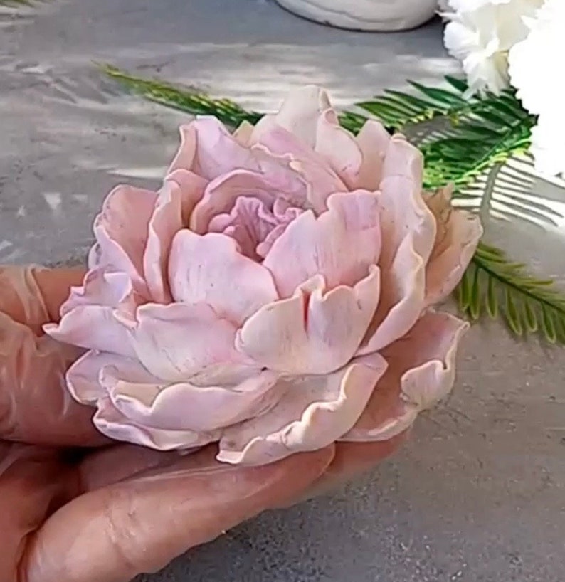 Pode incluir: Uma flor de pe&oacute;nia rosa p&aacute;lida delicada, feita &agrave; m&atilde;o com argila polim&eacute;rica. A flor tem um aspeto realista com detalhes intrincados e uma textura em camadas e com babados.