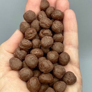 Op de afbeelding: Een handvol kleine, ronde, bruine chocolade snoepjes.