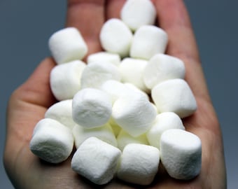 Può includere: Primo piano di una manciata di piccoli marshmallow bianchi. I marshmallow sono morbidi e soffici, con una forma rettangolare leggermente arrotondata. L'immagine evidenzia la consistenza e i dettagli dei marshmallow.