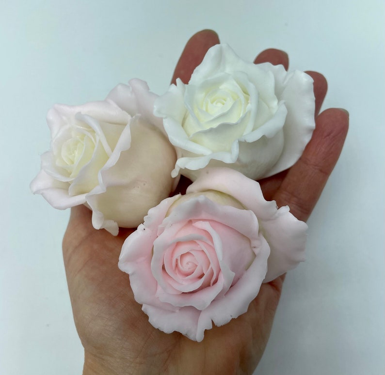 Pu&ograve; includere: Quattro rose di sapone fatte a mano, due bianche e due rosa, in una mano.