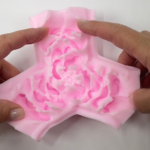 May include: Pink silicone mold shaped like a three-pointed star with a detailed peony flower design in the center.