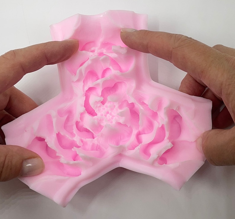 May include: Pink silicone mold shaped like a three-pointed star with a detailed peony flower design in the center.