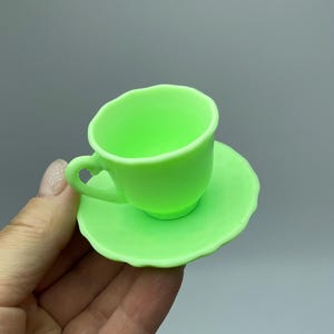 May include: A light green teacup and saucer set. The cup has a heart-shaped handle and the saucer has a scalloped edge.