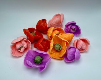 May include: A collection of handmade felt poppy flowers in various colors, including pink, orange, purple, and red. The flowers are all closed, with the petals folded inwards.