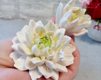 May include: Two white artificial dahlias with green centers. The flowers are made of a soft, pliable material and have a realistic appearance.