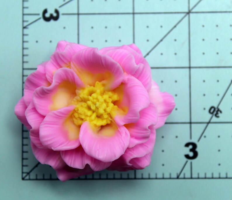 May include: A pink and yellow flower with a ruffled texture. The flower is made of polymer clay and has a realistic appearance.