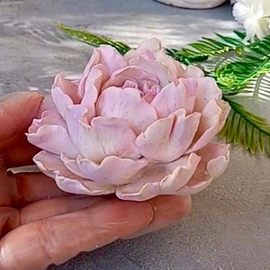 Pode incluir: Uma delicada flor de pe&ocirc;nia rosa feita &agrave; m&atilde;o com argila polim&eacute;rica. A flor tem uma apar&ecirc;ncia realista com detalhes intrincados e p&eacute;talas macias.