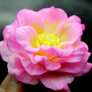 May include: A pink and yellow artificial flower with a ruffled texture. The flower has a yellow center with small yellow petals.