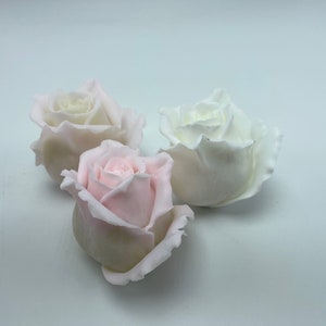Pu&ograve; includere: Tre boccioli di rosa artificiali, uno bianco, uno rosa chiaro e uno rosa scuro, sono disposti su una superficie bianca.