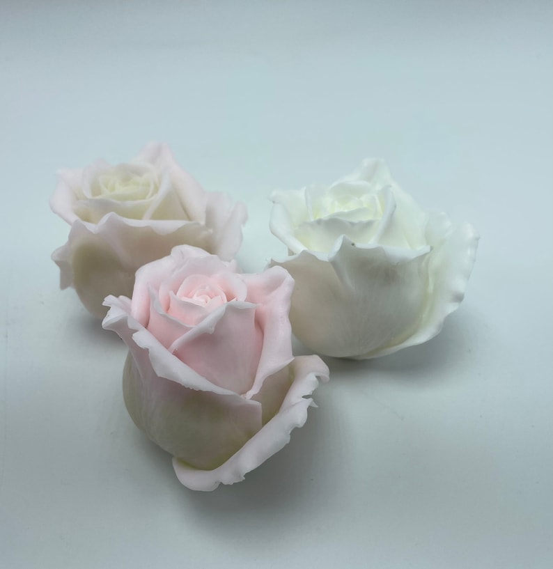 Pu&ograve; includere: Tre boccioli di rosa artificiali, uno bianco, uno rosa chiaro e uno rosa scuro, sono disposti su una superficie bianca.