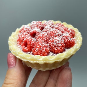 May include: A small, white, pie crust filled with red raspberries and topped with powdered sugar.