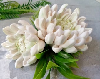 May include: A bouquet of white silk flowers with green leaves. The flowers are arranged in a cluster and have a delicate, realistic appearance.