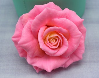 May include: A single pink rose with a light yellow center. The rose is made of a soft, pliable material and has a realistic appearance.