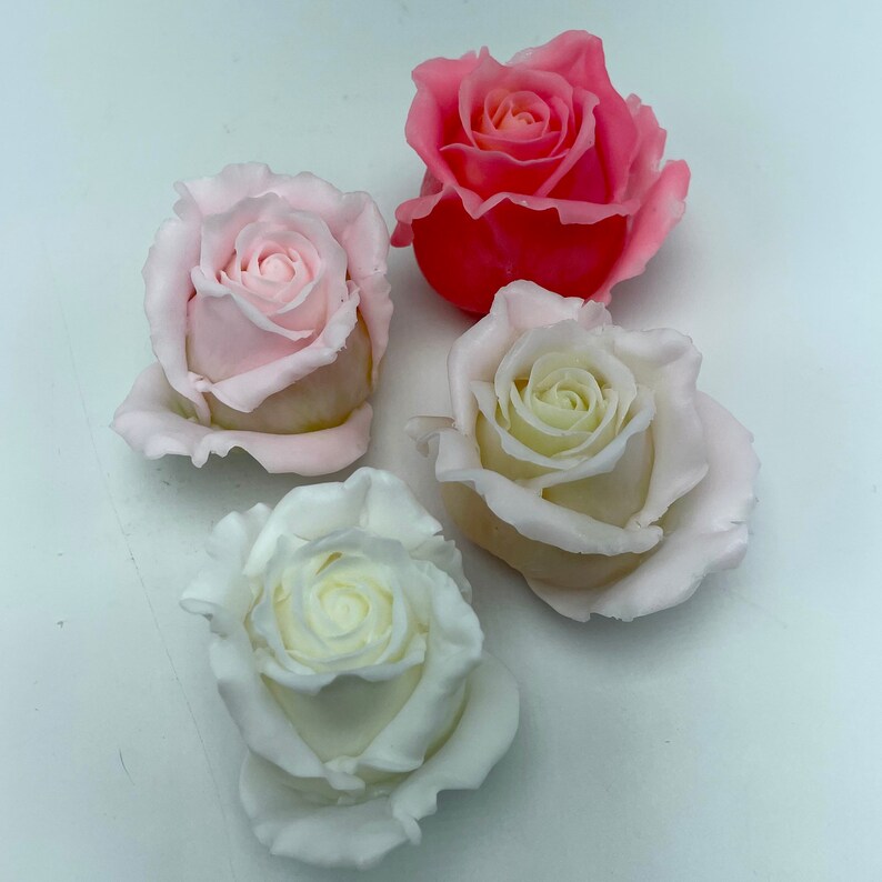 Pu&ograve; includere: Quattro rose di sapone fatte a mano in tonalit&agrave; di rosa e bianco. Le rose sono disposte su una superficie bianca.