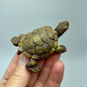 May include: A detailed miniature turtle figurine in brown and gold tones. The figurine has a textured shell and detailed legs and head. The turtle is a decorative item, possibly a collectible or home decor.