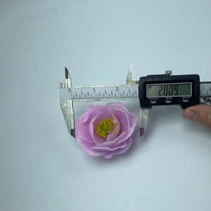 May include: A pink fabric flower with a yellow center, measured with a caliper to be 2.809 inches in diameter.