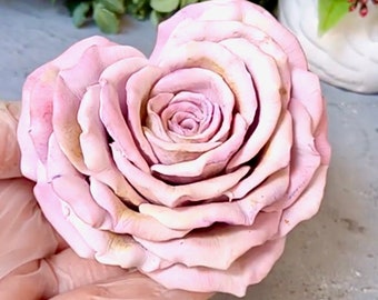 May include: A large, heart-shaped, pink rose made of fabric. The rose has many layers of petals and is a light pink color.