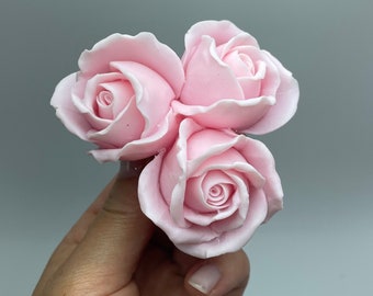 May include: Three pink artificial roses with a light pink center. The roses are arranged in a bouquet and held in a hand.