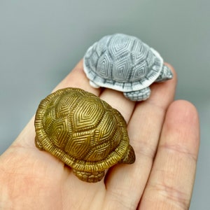 May include: Two small turtle figurines, one is gold and the other is white, both have a detailed geometric pattern on their shells.