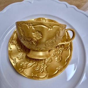 Könnte beinhalten: Ein goldfarbenes Tee-Set mit aufwendigen Blumenmustern. Das Set ist aus Keramik und hat eine glänzende Oberfläche.