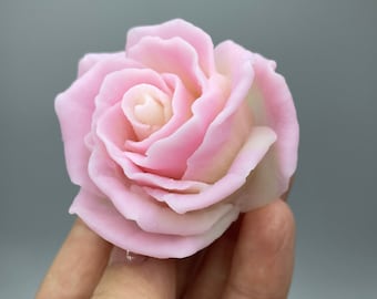 May include: A single pink rose made of soap. The rose is in a hand, but the hand is not visible in the image.