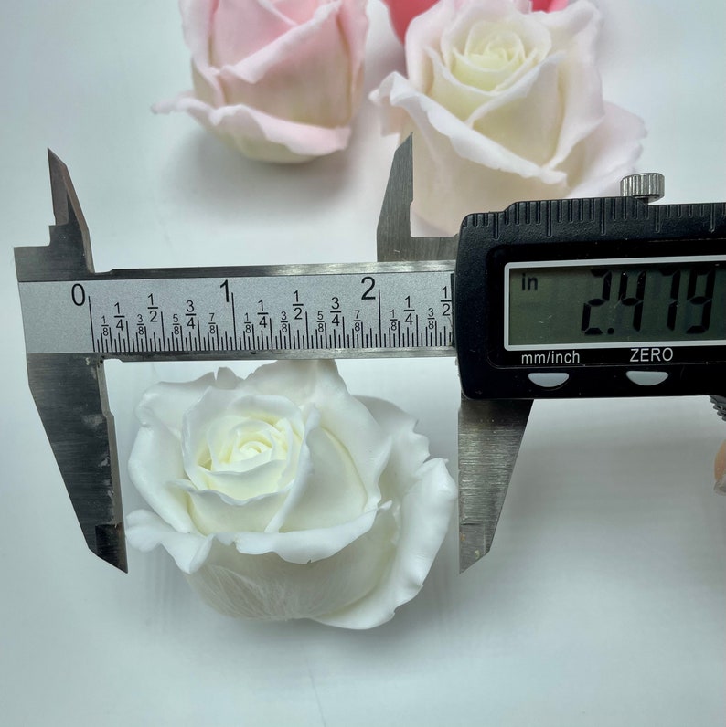 Pu&ograve; includere: Una rosa di tessuto bianco misurata con un calibro, che mostra una misura di 2,79 pollici.