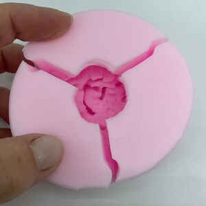 May include: Pink silicone mold with three sections, designed for creating round objects with a center hole.