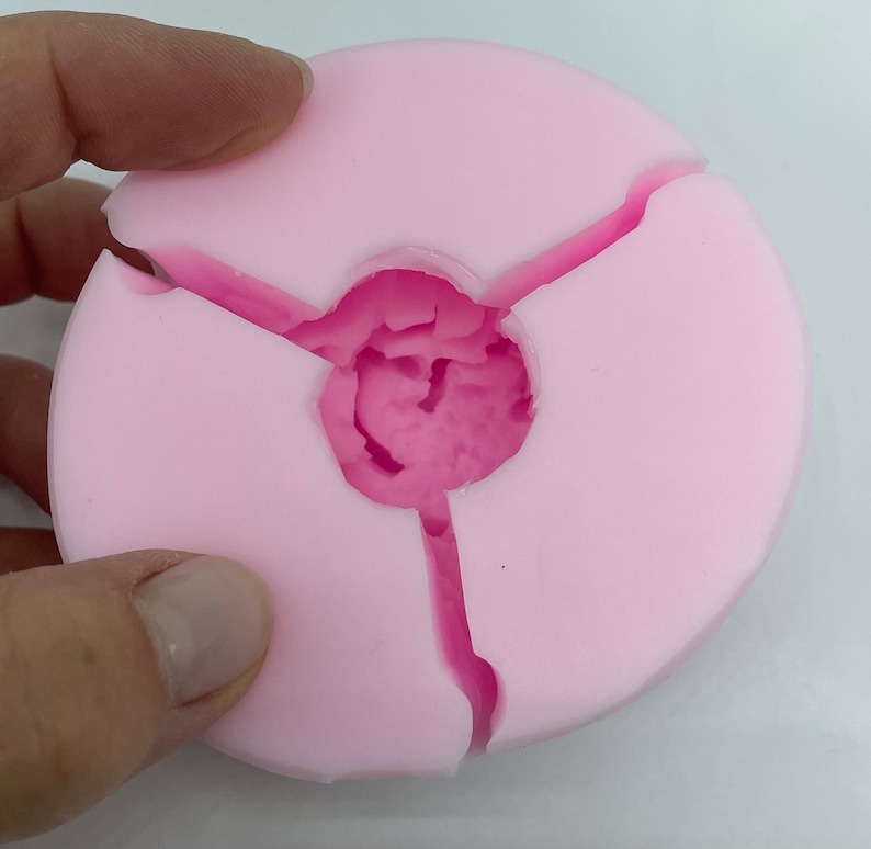 May include: Pink silicone mold with three sections, designed for creating round objects with a center hole.