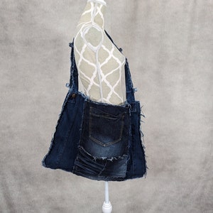 May include: A blue denim tote bag made from repurposed denim fabric. The bag has a large pocket on the front and a frayed edge.