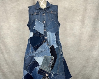May include: A sleeveless denim dress with a patchwork design. The dress has a collared neckline, button-down front, and a mix of light and dark blue denim patches. The dress is displayed on a white mannequin.