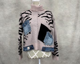May include: A pale pink turtleneck jumper with black tiger stripes and denim patches. The jumper has a black square patch and several denim patches sewn onto the front. The jumper is displayed on a white mannequin head.