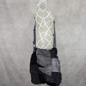 Peut inclure: Un sac fourre-tout en denim patchwork gris et noir avec une poche zippée et une bandoulière. Le sac est sur un mannequin blanc.