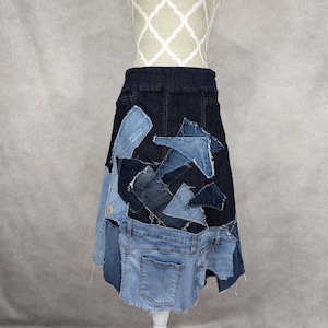 Peut inclure: Une jupe en jean bleu foncé avec un motif patchwork réalisé à partir de différentes nuances de denim bleu. La jupe a une silhouette droite et un ourlet effiloché.