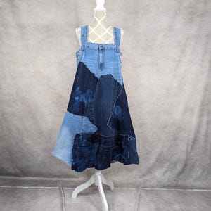 May include: A long denim dress made from patchwork denim fabric in shades of blue. The dress has a sleeveless design with adjustable straps and a flowing skirt.