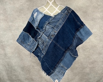 May include: A denim poncho made from recycled denim fabric. The poncho is blue and has a patchwork design. It is displayed on a white mannequin.