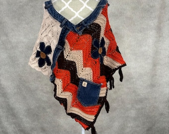 May include: A crocheted poncho with a denim design. The poncho is made with brown, orange, and white yarn and features two denim pockets and two flower appliques.