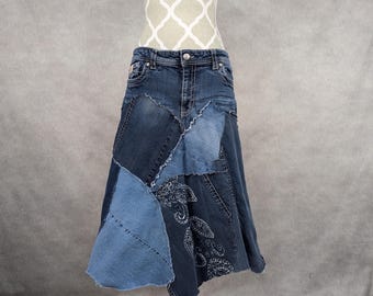 May include: A denim skirt made from patchwork denim with a paisley design. The skirt is a-line and falls to the knees.