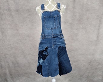 May include: A denim overall skirt with a patchwork design. The skirt is blue and has a frayed hem.
