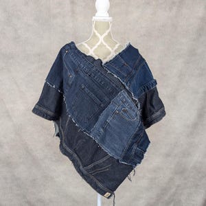 Puede incluir: Un poncho de mezclilla hecho de tela de mezclilla reutilizada. El poncho es un mosaico de diferentes tonos de mezclilla azul y tiene un borde deshilachado.