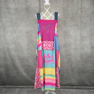 May include: A long, patchwork dress with a pink, blue, yellow, and rainbow colour scheme. The dress has a variety of patterns, including flowers, stripes, and a palm tree design. The dress has the text "Hello Gorgeous" printed on it.