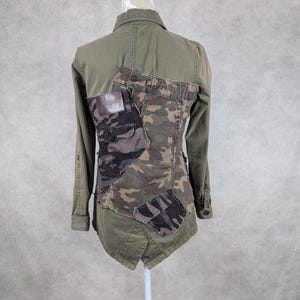 Könnte beinhalten: Eine grüne Utility-Jacke mit einem Tarnmuster auf dem Rücken. Die Jacke hat einen Knopfschließer vorne und lange Ärmel.